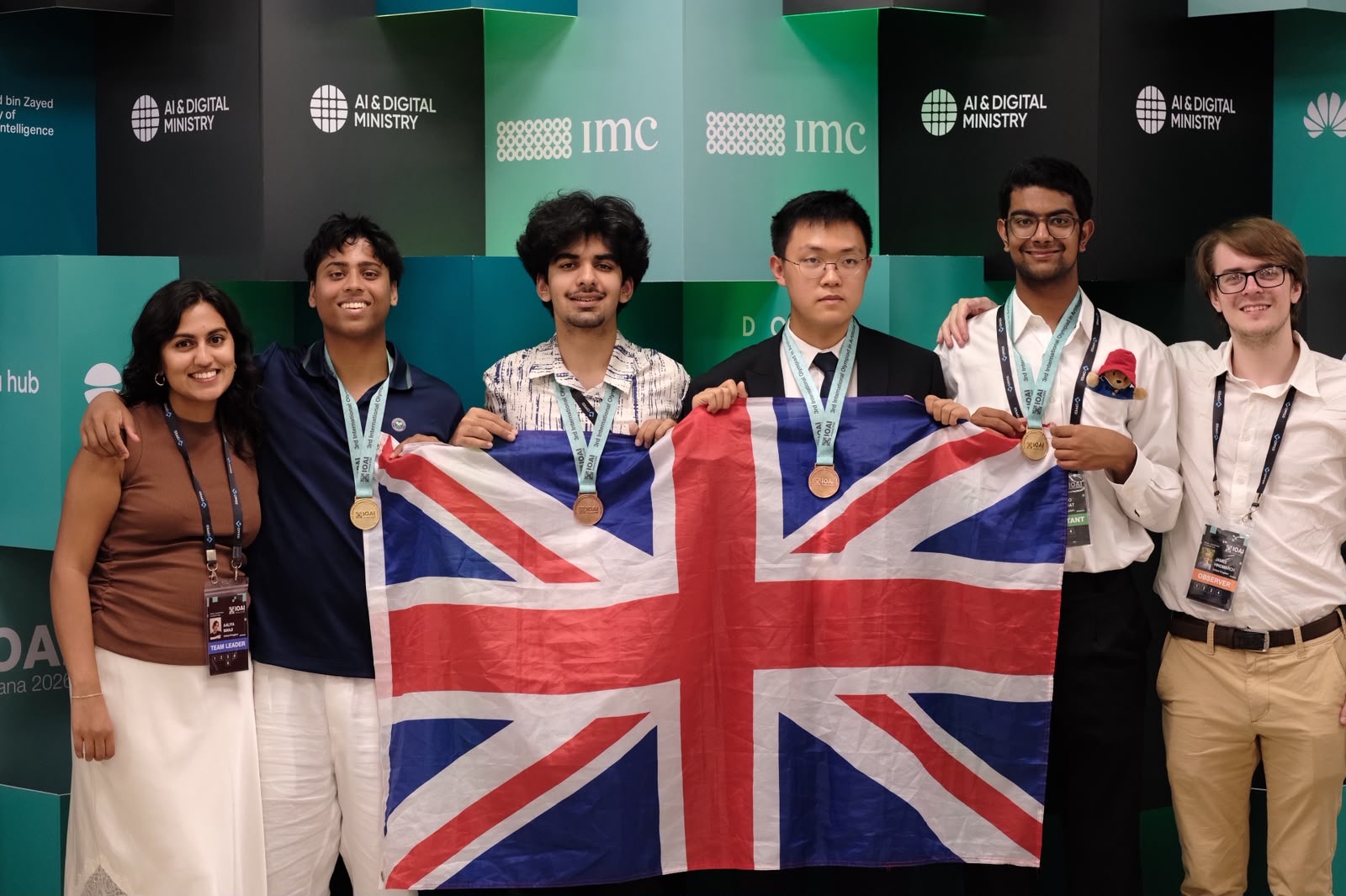The UK team and leaders holding a Union flag at the International Olympiad in AI 2026 in Astana, the four contestants wearing their medals